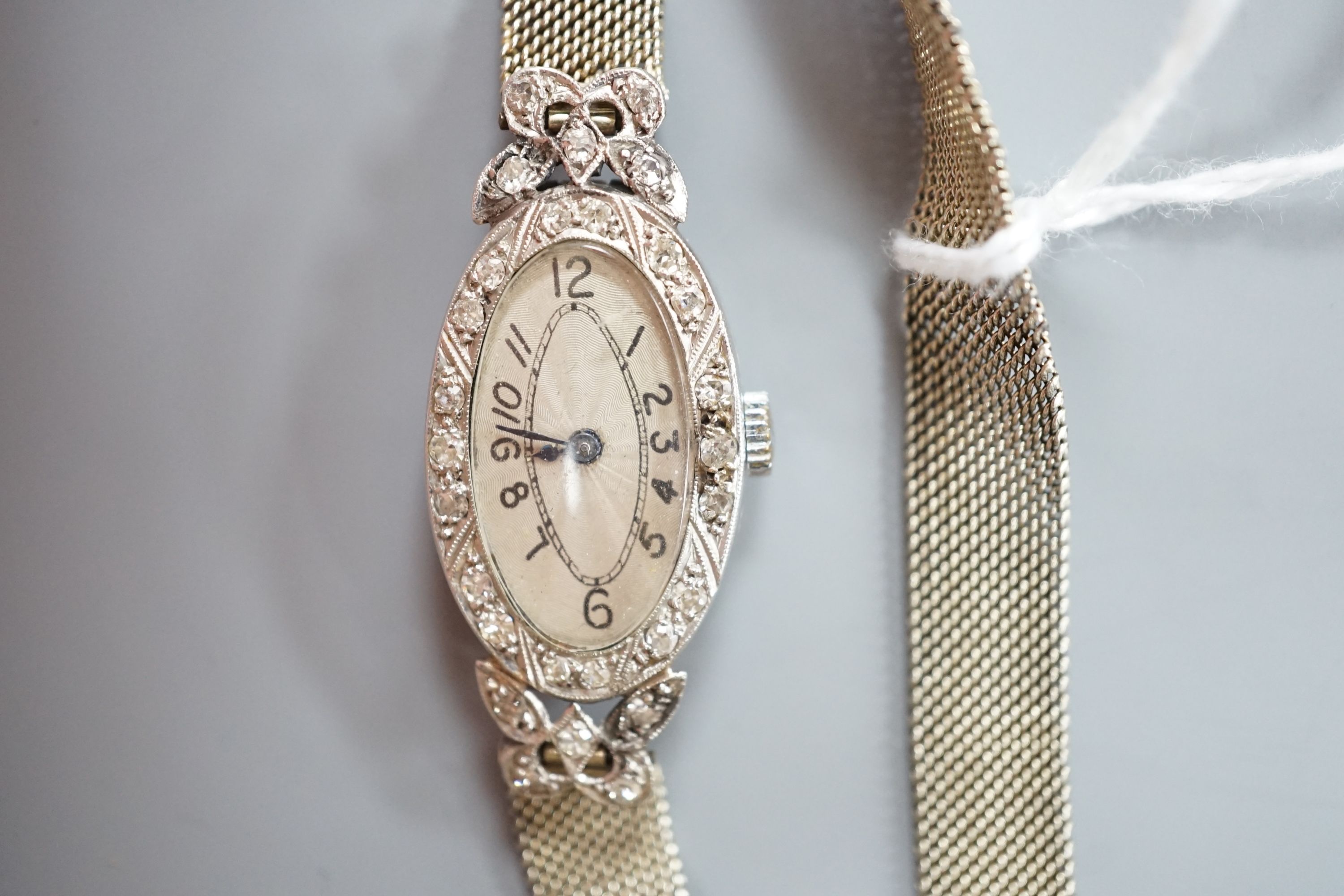 A lady's mid 20th century white metal (stamped platinum) and diamond set manual wind oval cocktail watch, on a white metal mesh bracelet stamped '18', gross weight 21.6 grams.